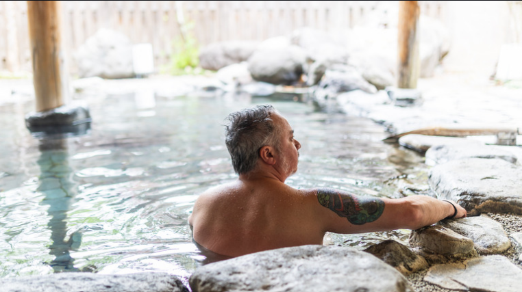 Homme avec un tatouage au bras dans un onsen en plein air au Japon, où les tatouages sont souvent refusés