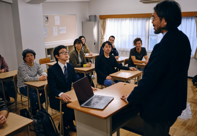 A Japanese teacher giving a lecture to a diverse group of students in a classroom at a vocational school (senmon gakkou) in Japan.