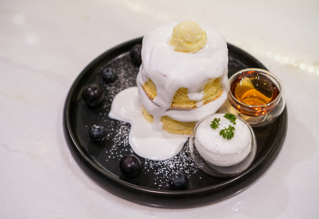 Plate of fluffy pancakes topped with whipped cream, served with blueberries, ice cream, and syrup.