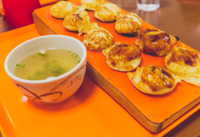 Akashiyaki, a traditional Kansai dish, served with dipping broth on an orange tray in Kobe.