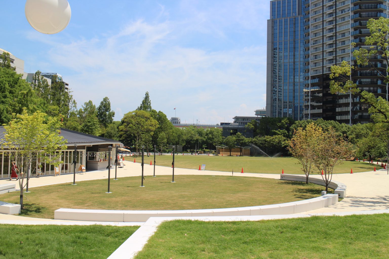 Exterior view of Communica Institute campus in Kobe, Japan, with a green lawn and modern city buildings in the background.