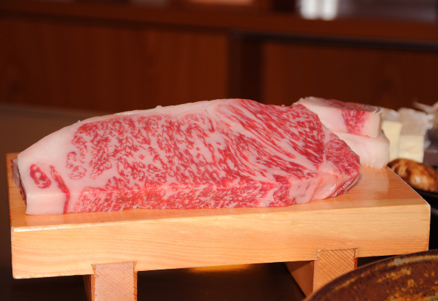 Raw Kobe beef steak with rich marbling, displayed on a wooden board at a restaurant.