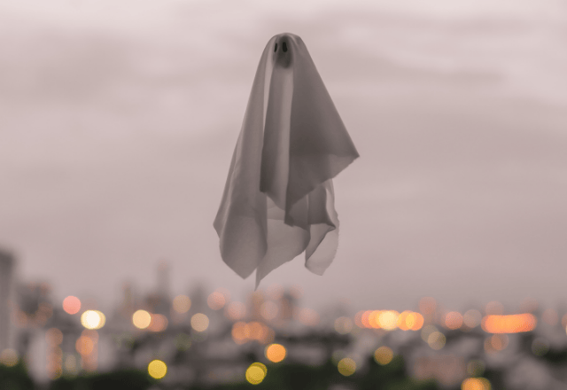 A playful ghost-like figure resembling a traditional Yokai, floating above a cityscape at dusk, with glowing city lights in the background.