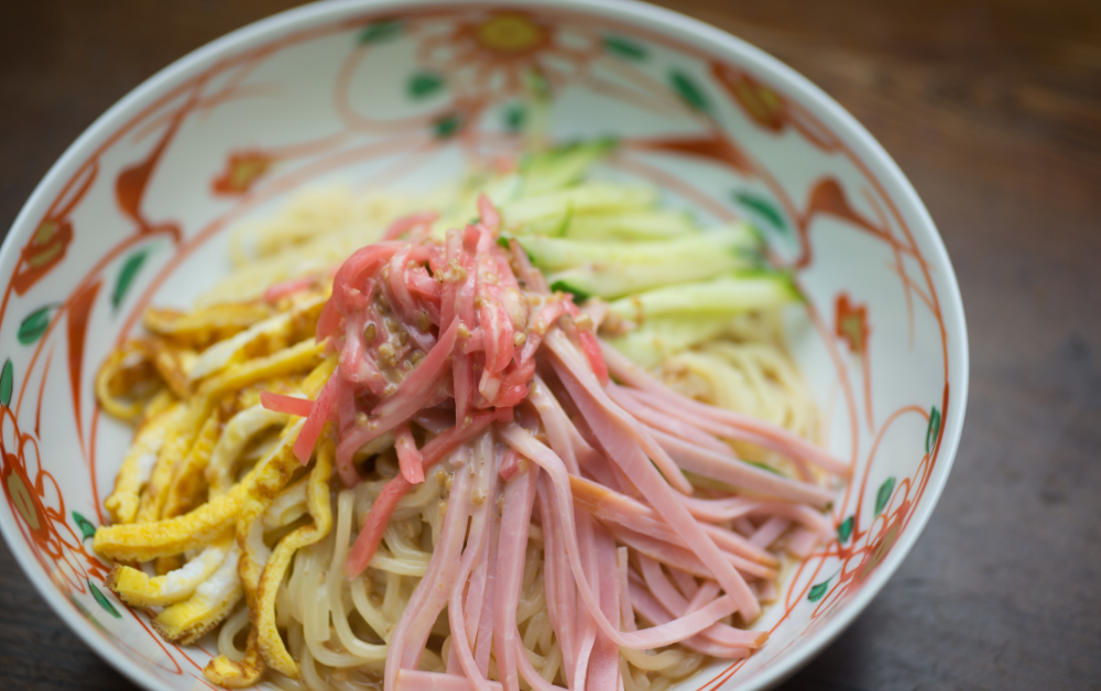 Hiyashi Chūka (冷やし中華) – cold ramen topped with sliced cucumber, ham, egg, and tomato, served with a tangy soy-vinegar dressing.
